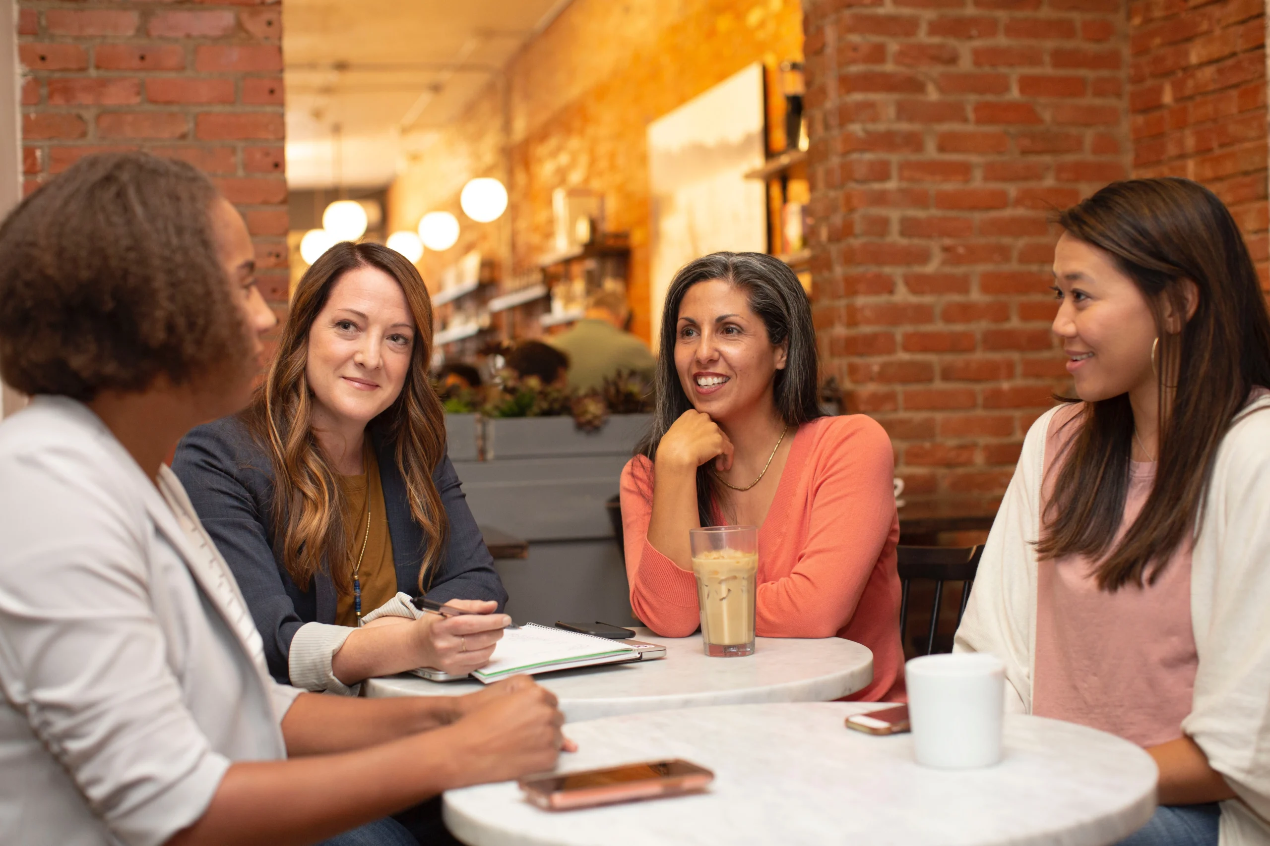 Women mentoring Women in Leadership Development around a small table with coffee cups, phones and a notebook on the table.