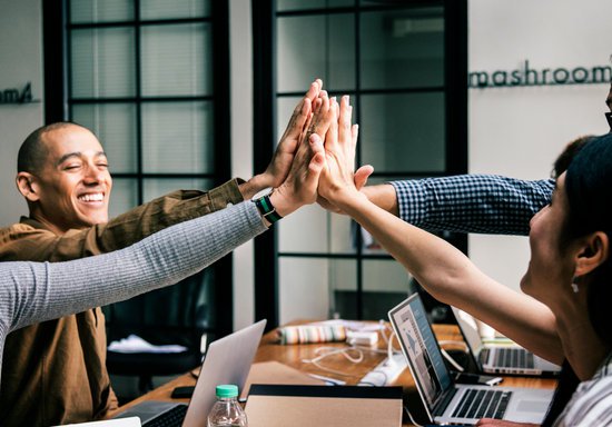 Team of coworkers high five together with each other to celebrate.