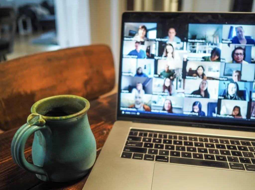 Home office setting. Turquoise clay coffee mug sitting beside an open laptop. Laptop is displaying a virtual mentoring meeting with other mentors and mentees.