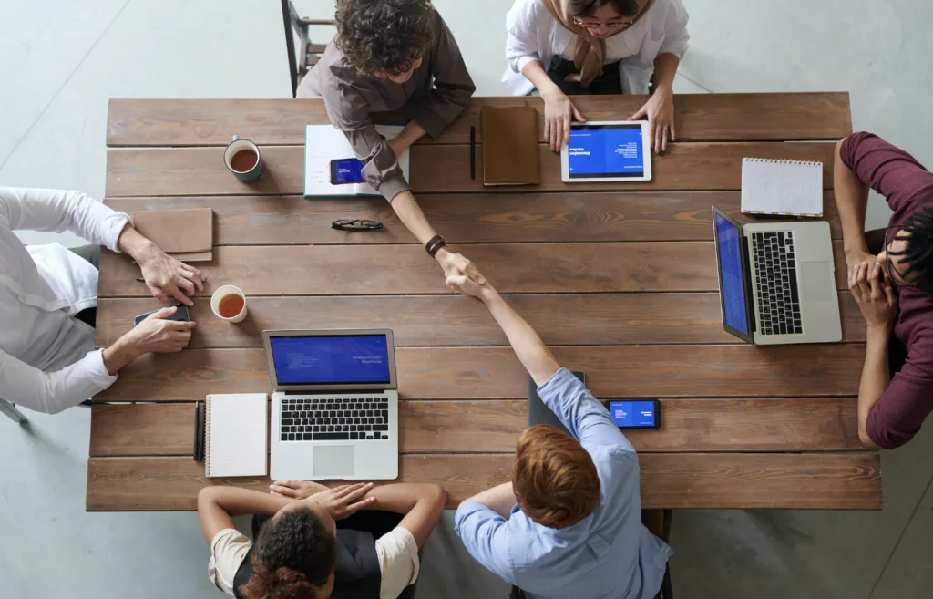 Workers at a table shaking hands after knowledge sharing. 