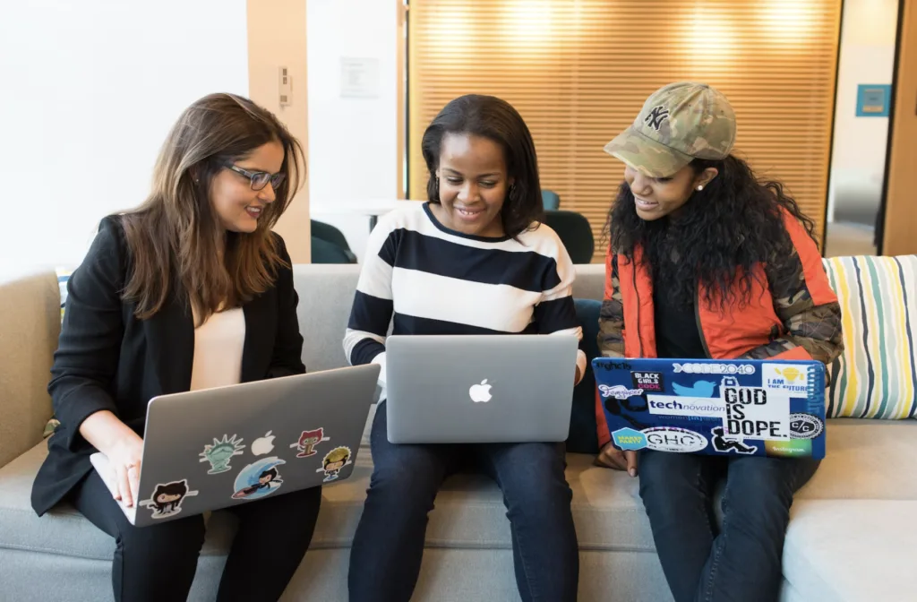 Women on a coach looking at computers while networking in a sales mentoring relationship. 