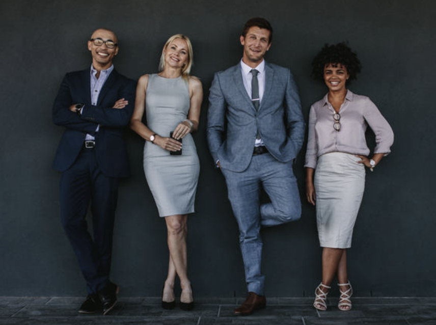 Four business people smiling and leaning up against a wall