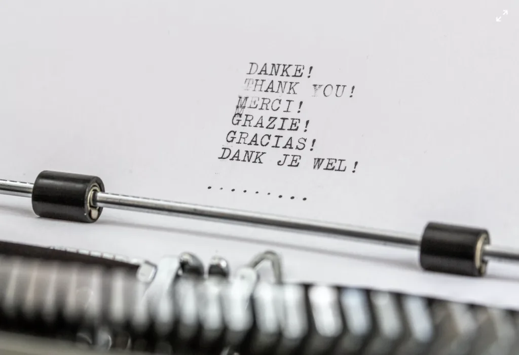 Paper in a typewriter that has the words thank you typed in different languages 