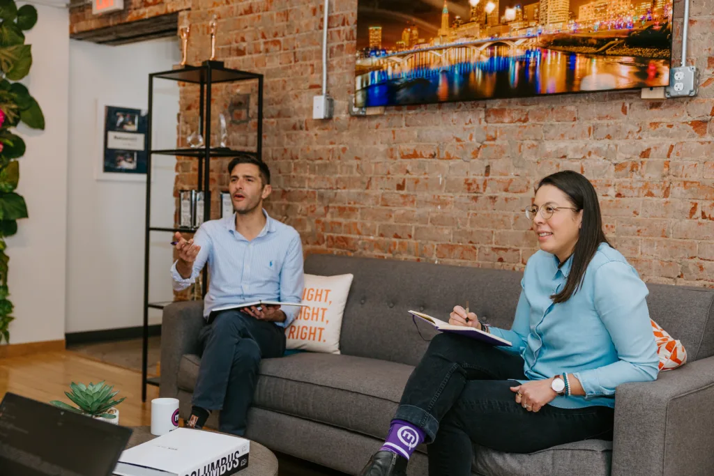 Team members in an office on a couch using bias for action to boost productivity.