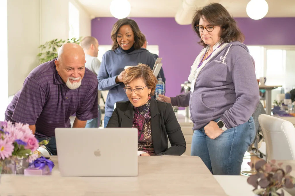 Image of diverse team members in an inclusive work space looking at a computer together.