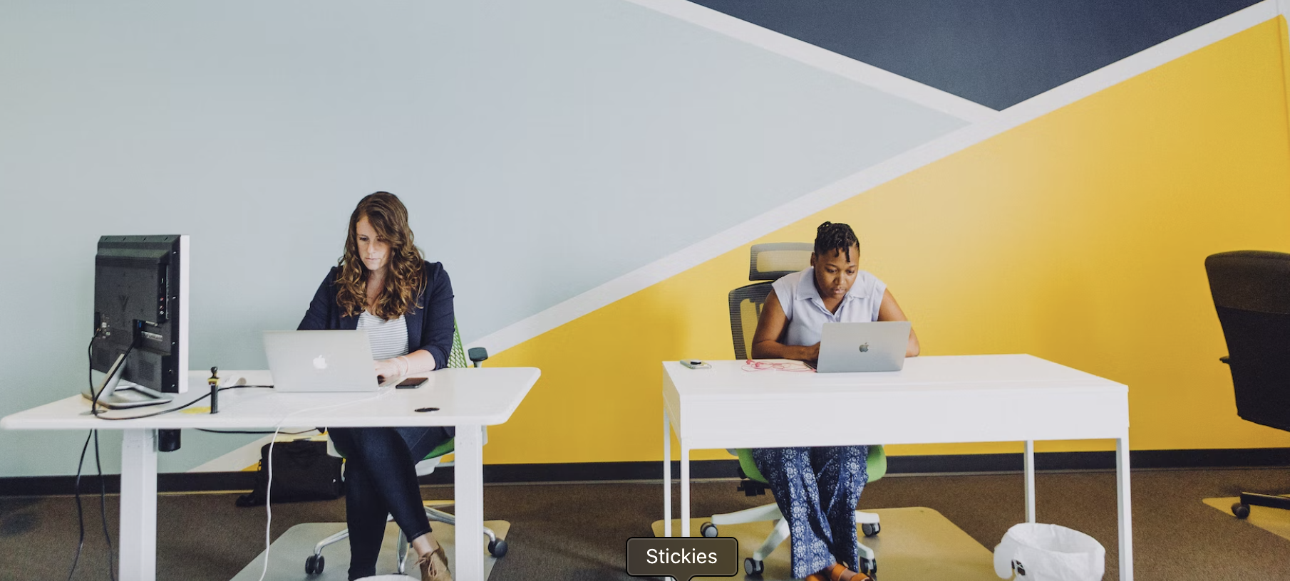 Women working together behind a mutli-colored background of geometric shapes.