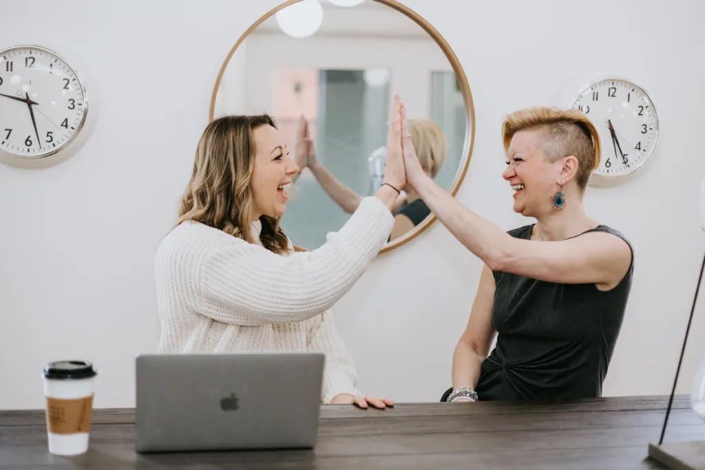 Two women high fiving at a desk.