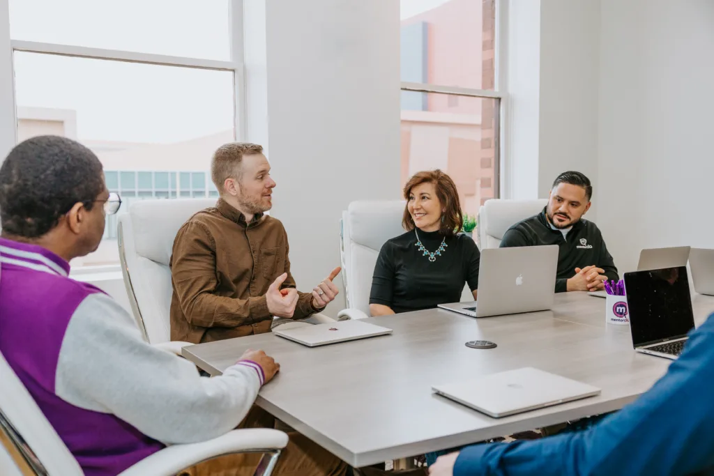 Employees in a group mentoring setting sit around a table in a discussion. 