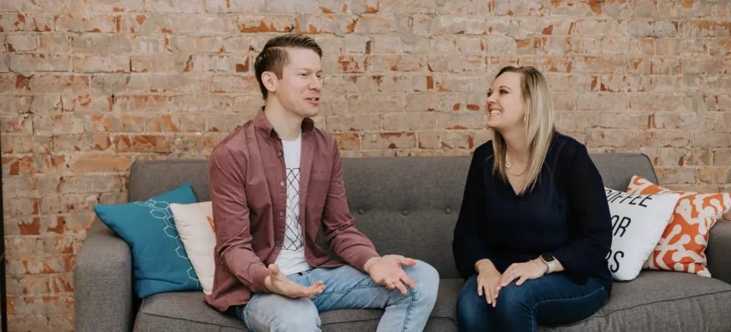 An image of employees happily in the workplace on a couch chatting.